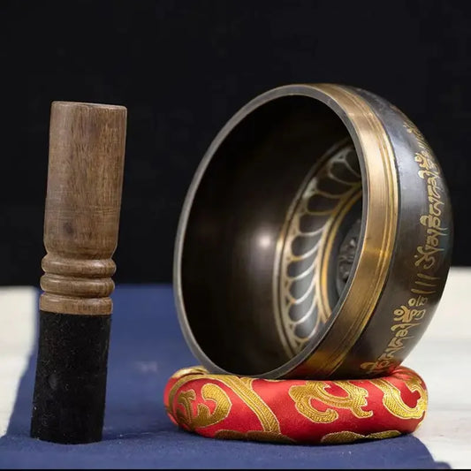 A handcrafted Tibetan singing bowl made of bronze alloy, displayed with a wooden mallet and a red cushion.